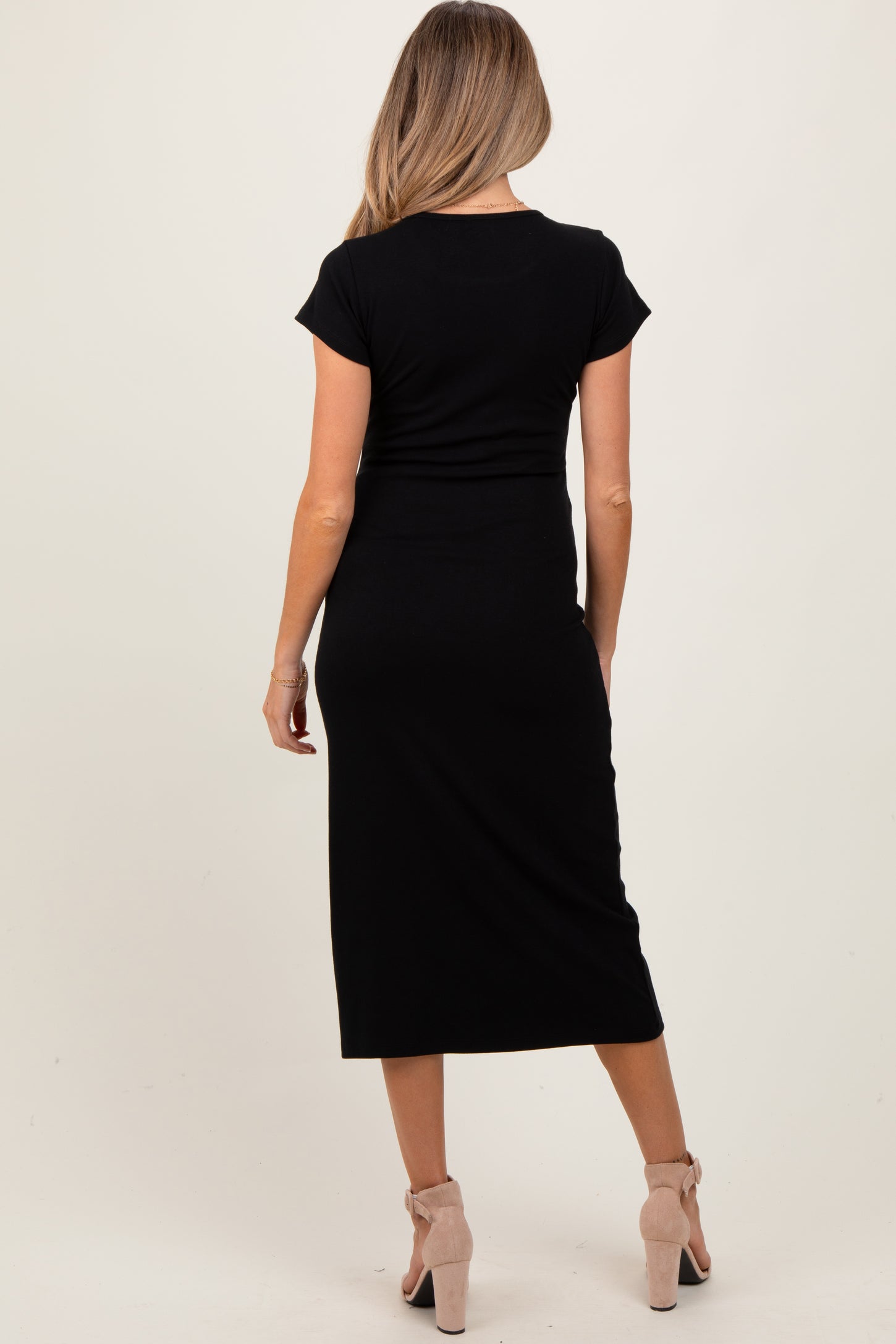 woman wearing a black short sleeve maternity dress with a midi length, showing her back and styled with beige heels