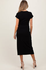 woman wearing a black short sleeve maternity dress with a midi length, showing her back and styled with beige heels