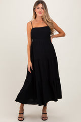 woman wearing a black maternity maxi dress with spaghetti straps and a tiered skirt, showcasing her baby bump