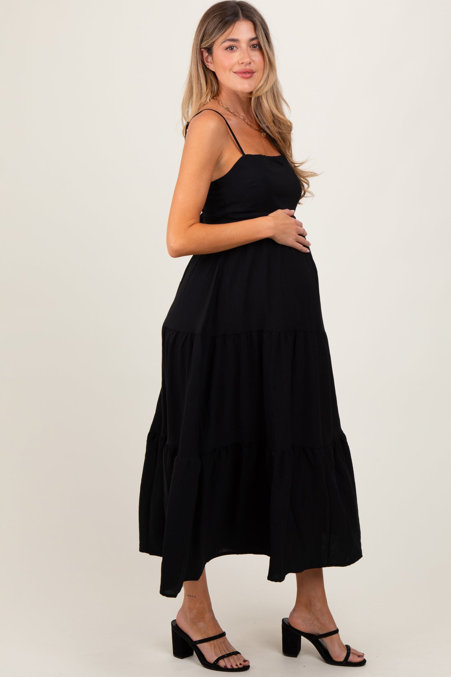 woman wearing a black tiered maternity dress and holding her baby bump
