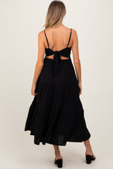 woman wearing a black maternity maxi dress with a tie-back detail and tiered skirt, showing a baby bump