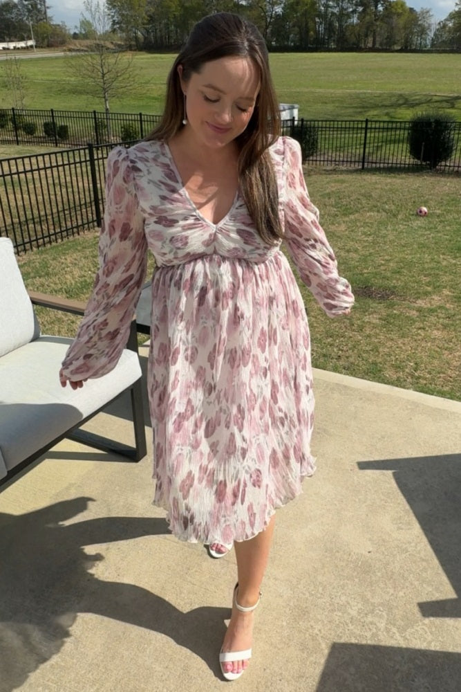 woman wearing a floral patterned long sleeve dress with a v-neckline and a flowy hem, standing outdoors on a sunny day