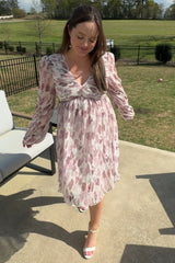 woman wearing a floral patterned long sleeve dress with a v-neckline and a flowy hem, standing outdoors on a sunny day