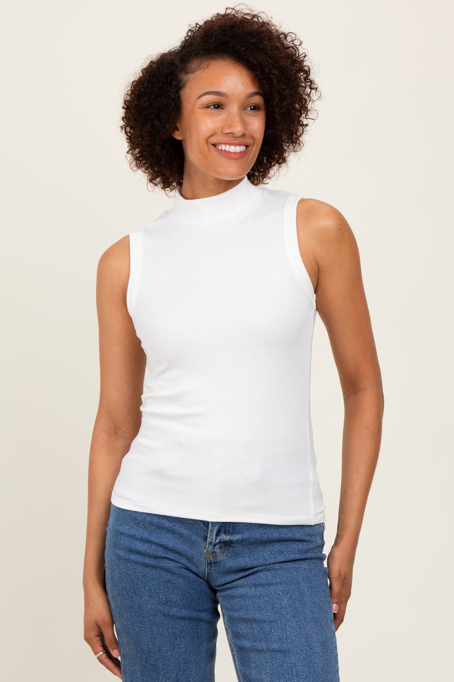 woman wearing a white sleeveless mock neck top with a fitted style and curly hair