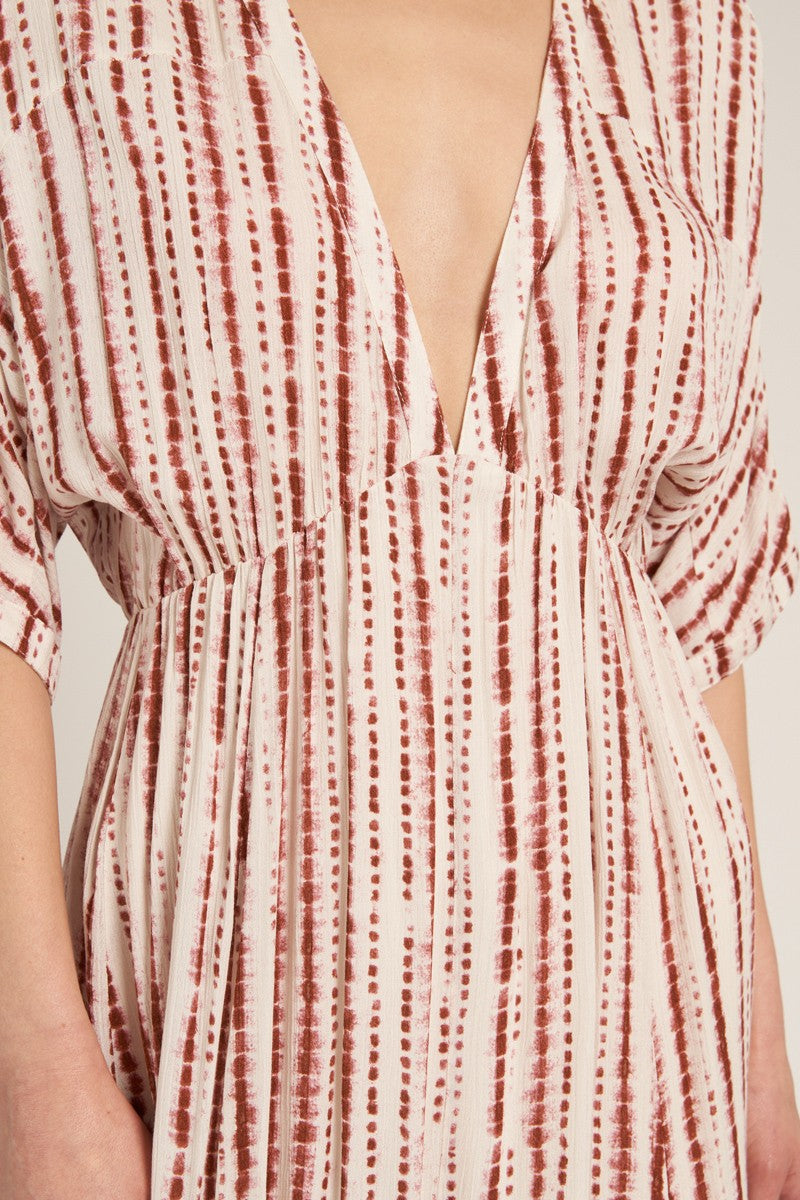 woman wearing a patterned deep v-neck midi dress with short sleeves and flowing fabric in shades of cream and rust