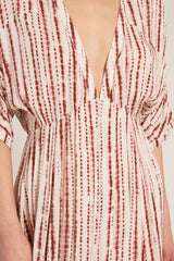 woman wearing a patterned deep v-neck midi dress with short sleeves and flowing fabric in shades of cream and rust