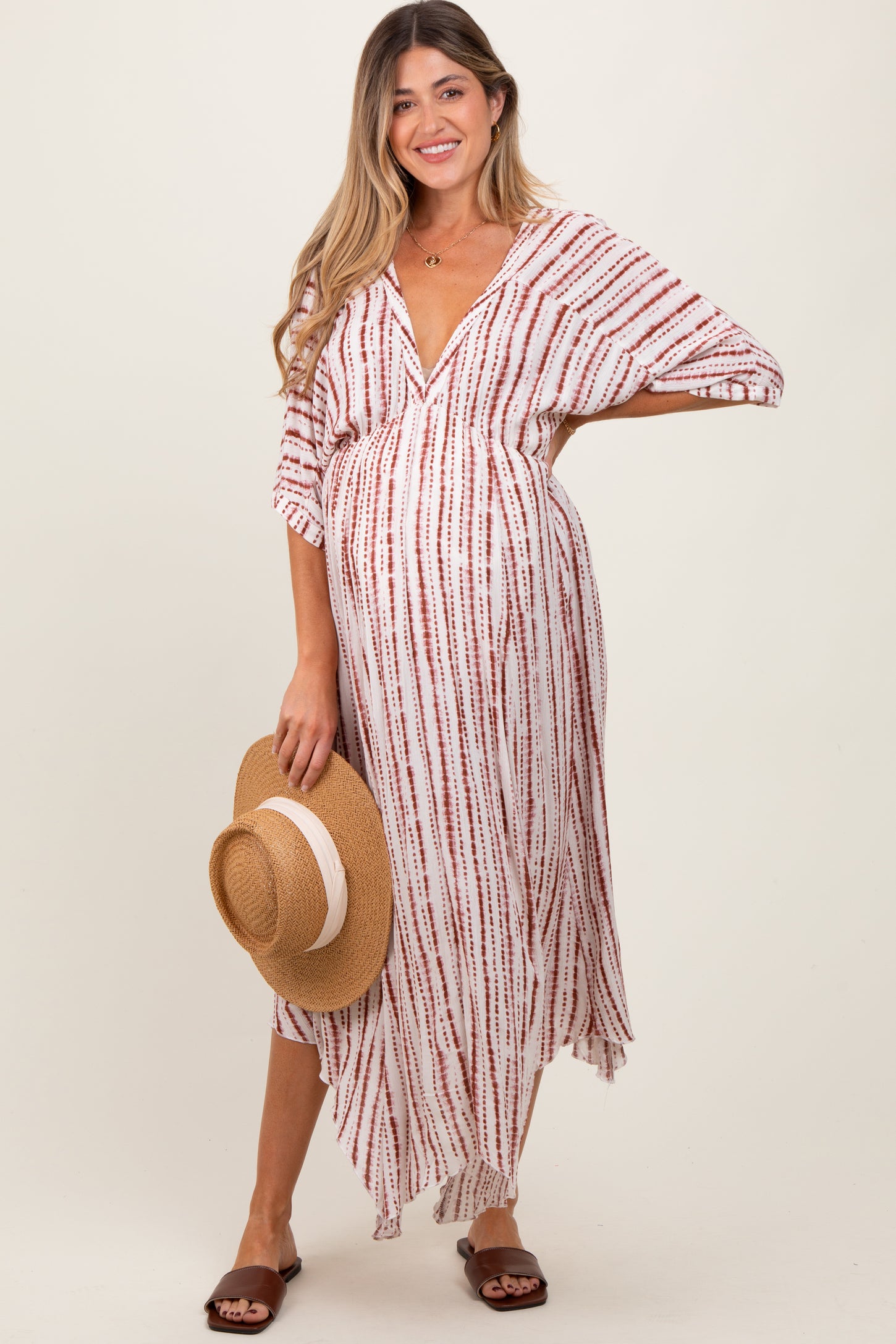 woman wearing a red and white striped maternity maxi dress and holding a straw hat, showcasing her baby bump
