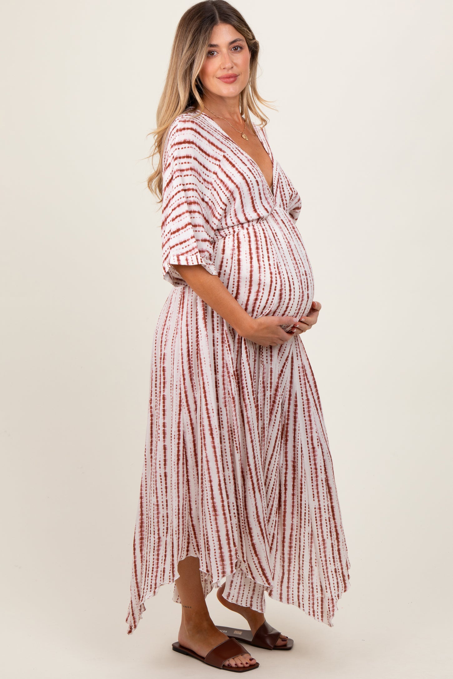 woman wearing a red and white striped maternity maxi dress with a deep v-neck and holding her baby bump