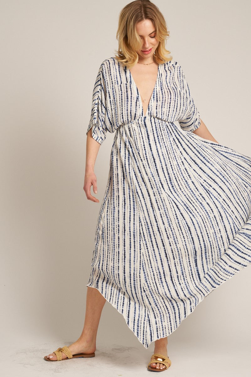 woman wearing a flowy white maxi dress with navy stripes and a deep v-neck, standing in a playful pose