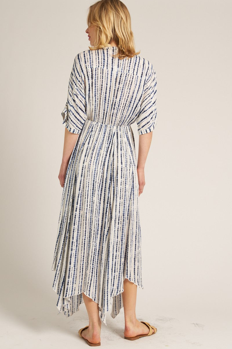 woman wearing a back view of a white and blue striped maxi dress with an asymmetrical hem and three-quarter sleeves