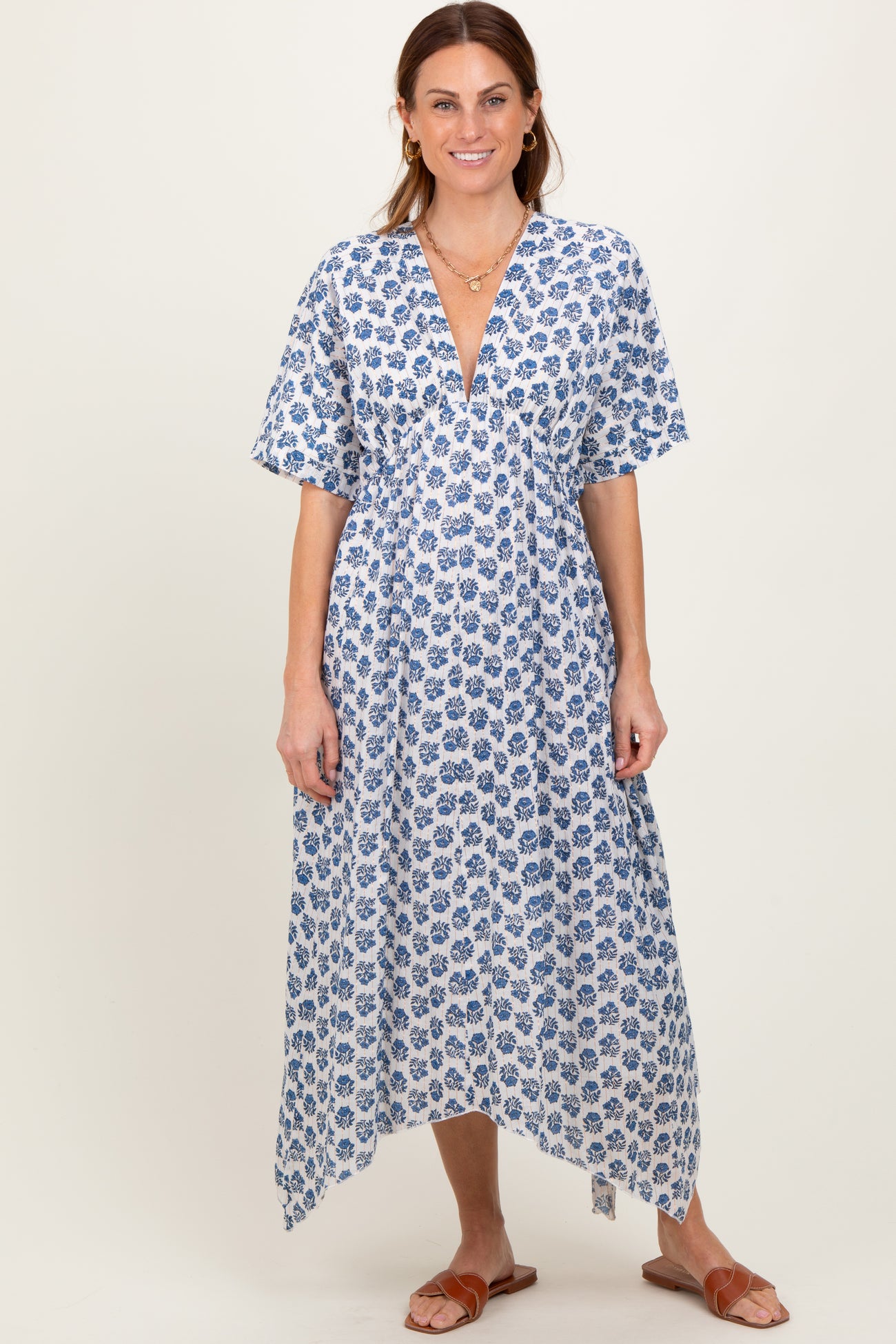 woman wearing a flowy white dress with blue floral print and a deep V-neck, standing and smiling