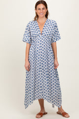 woman wearing a flowy white dress with blue floral print and a deep V-neck, standing and smiling