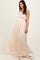 woman wearing a beige maxi dress with intricate lace detailing and a flowy skirt, standing in a relaxed pose