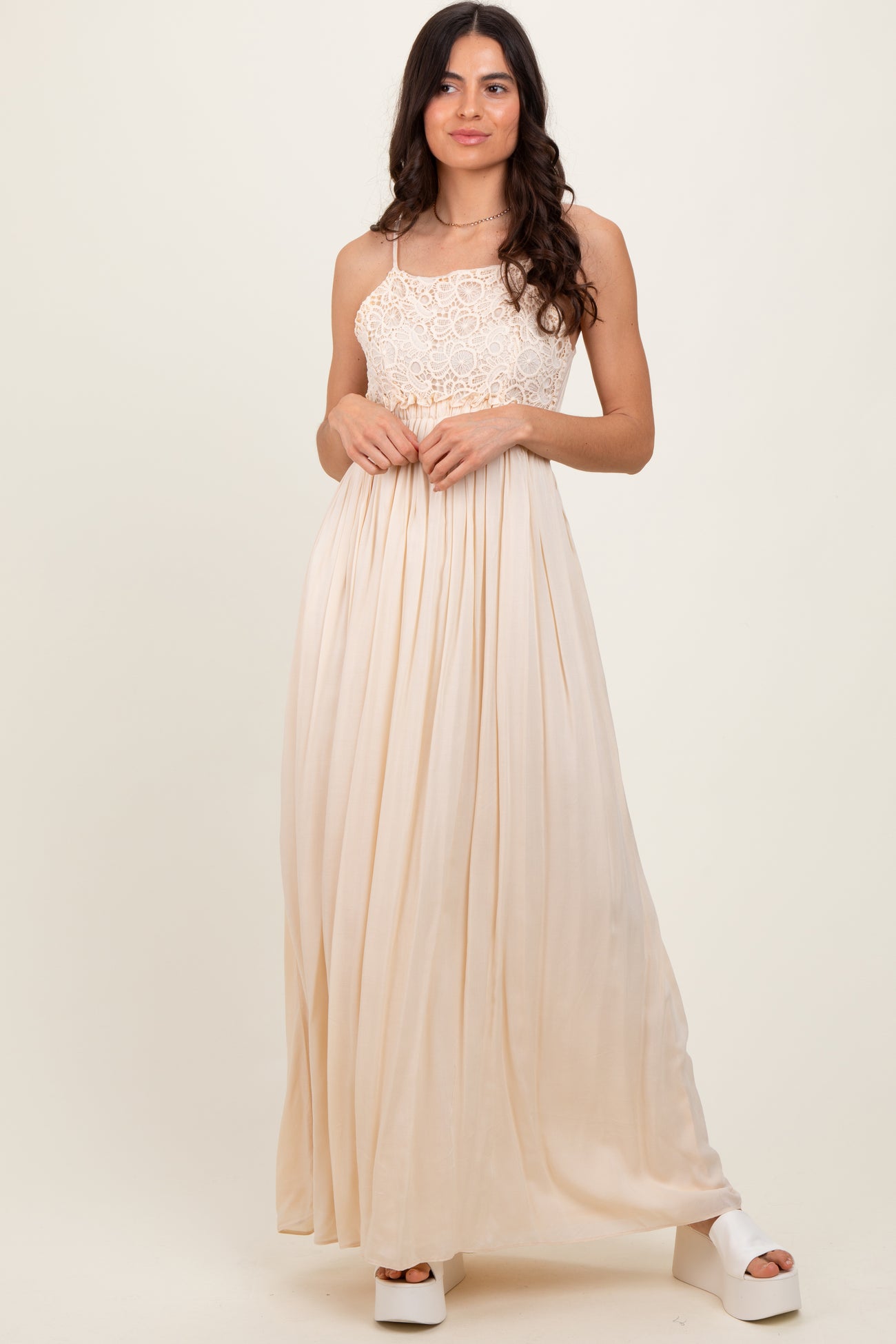 woman wearing a cream lace bodice maxi dress with a flowing pleated skirt and platform heels