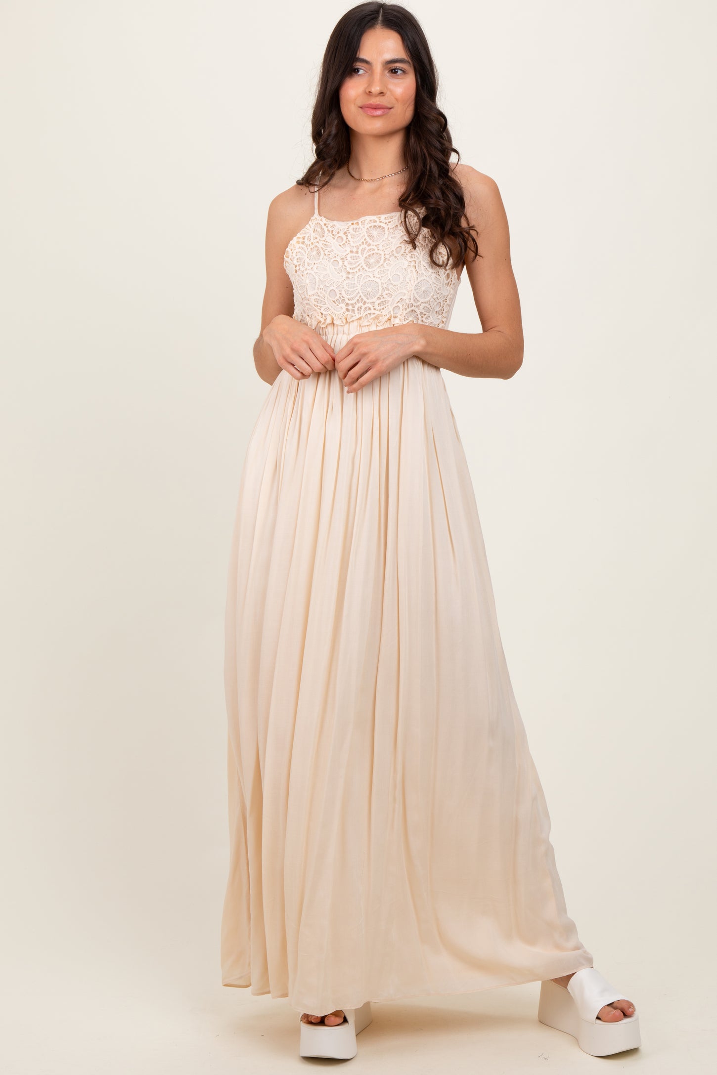 woman wearing a cream lace bodice maxi dress with a flowing pleated skirt and platform heels