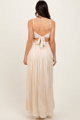 woman wearing a backless light beige maxi dress with a tied bow detail and pleated skirt