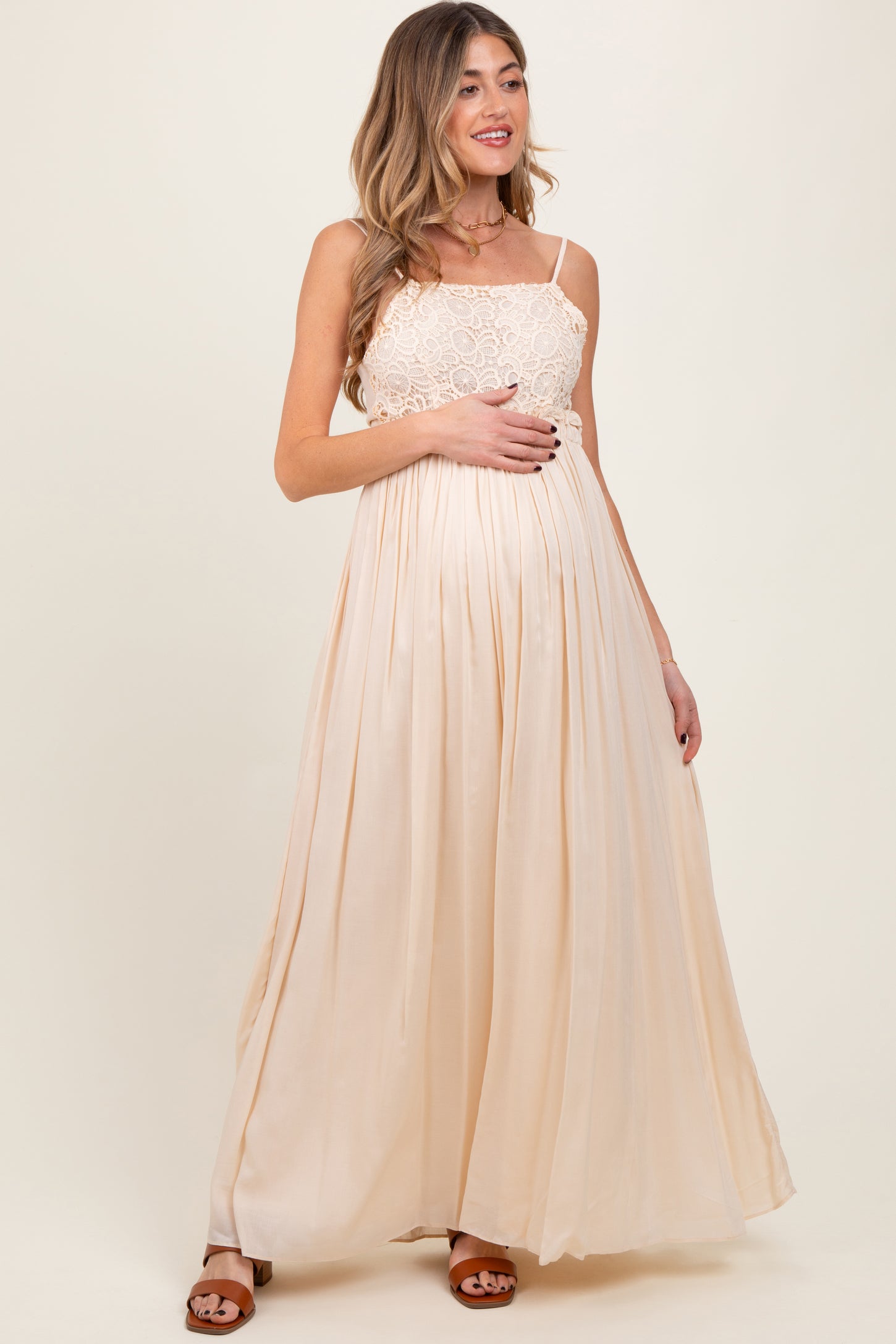 woman wearing a beige lace bodice maternity maxi dress and holding her baby bump