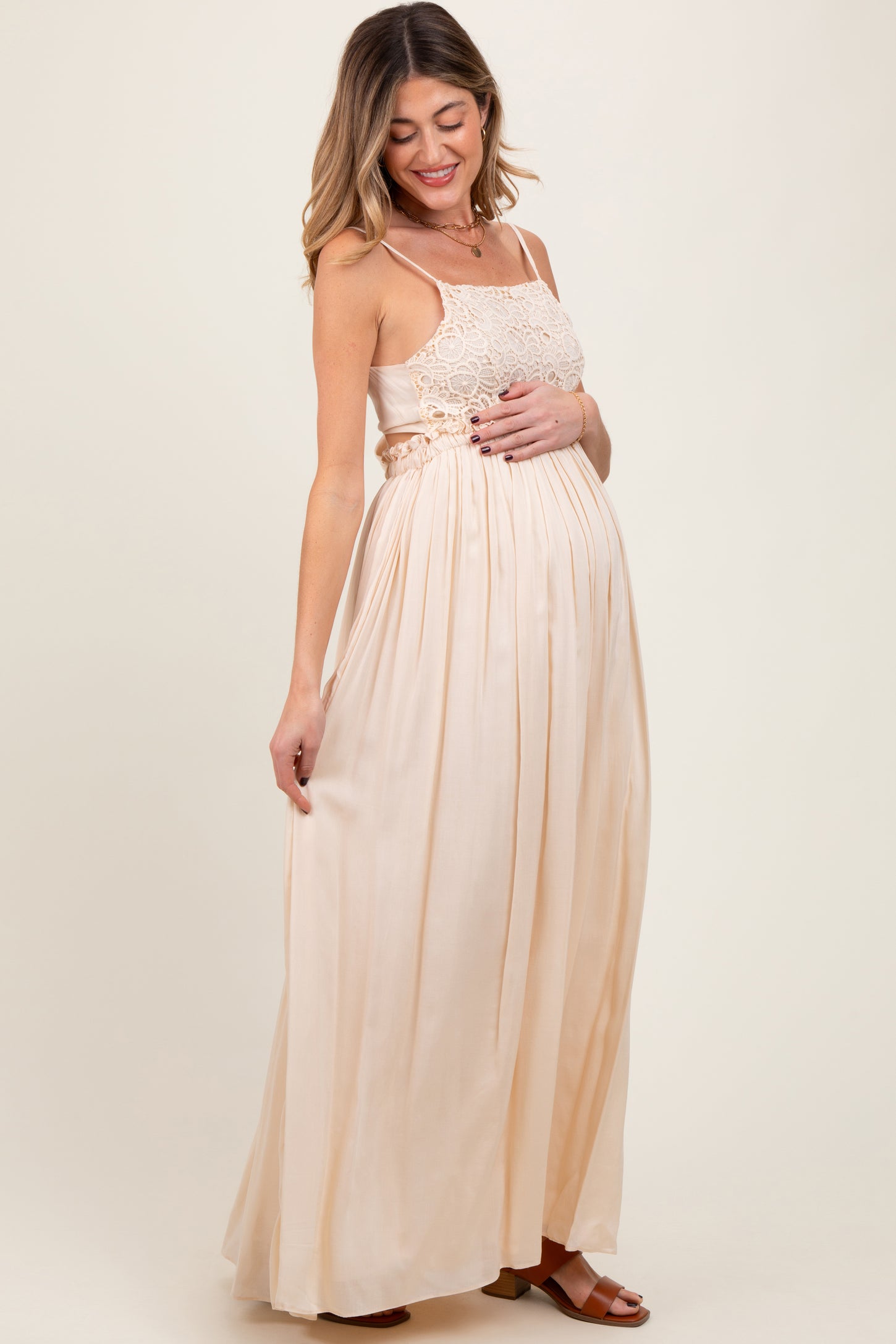 woman wearing a light peach maternity maxi dress with lace detailing, gently cradling her baby bump