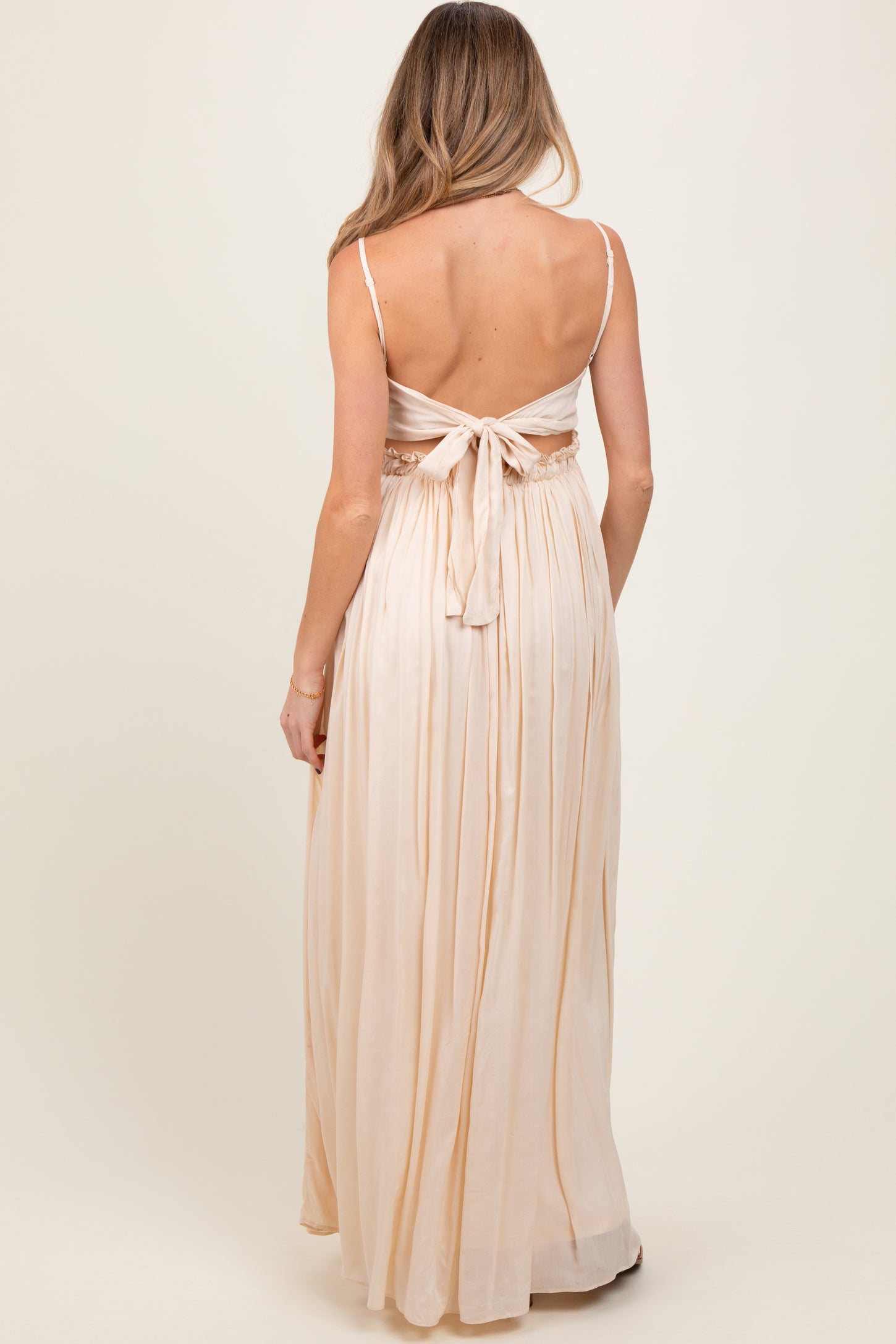 woman wearing a light peach maternity maxi dress with a tie back and flowing skirt, seen from the back