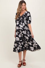woman wearing a black floral maternity dress with puff sleeves and a flowing skirt, showcasing her baby bump