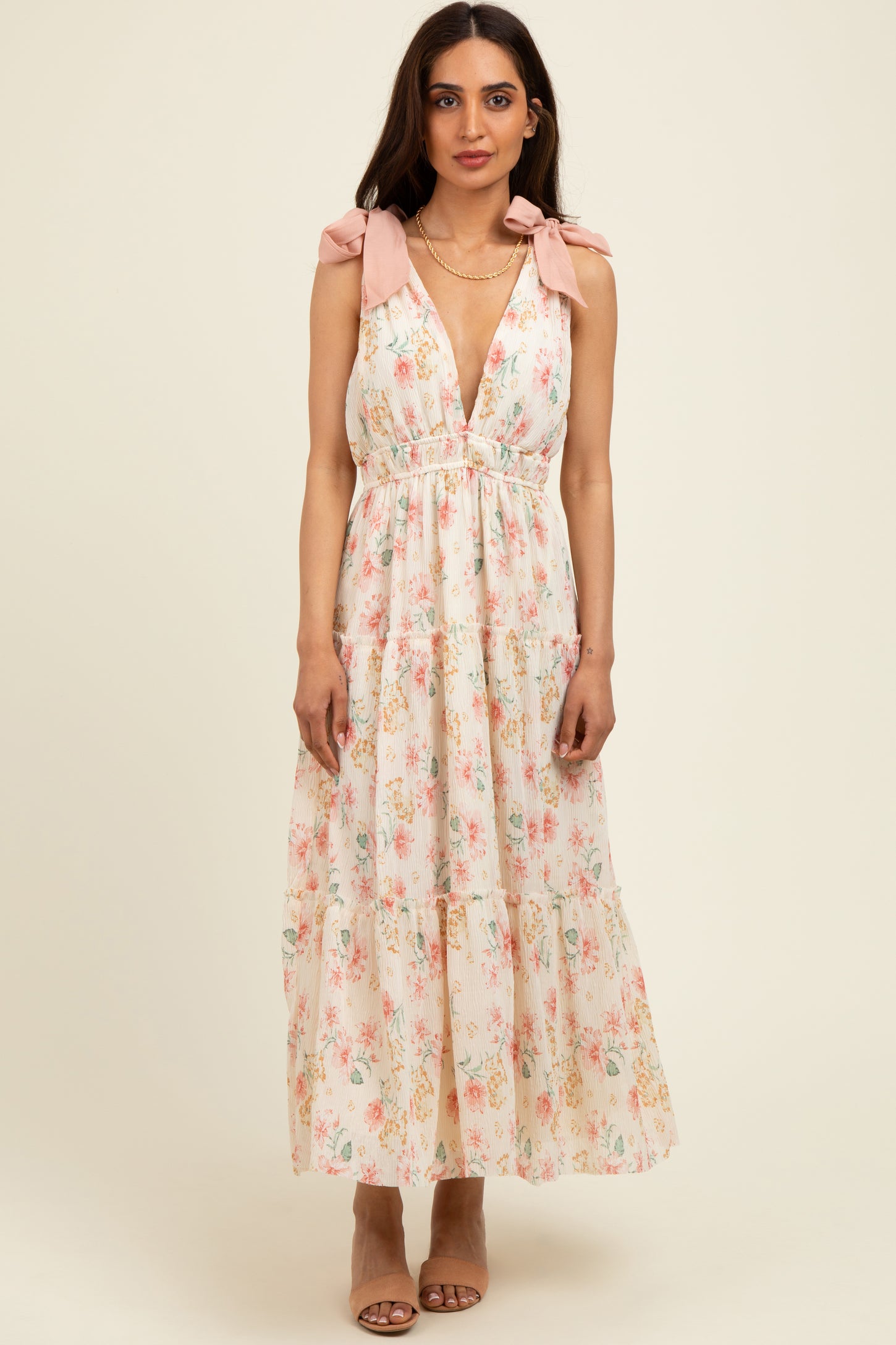 woman wearing a floral maxi dress with pink tie straps and a plunging neckline, standing against a neutral background