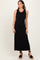 woman wearing a black sleeveless maxi dress with a textured fabric and standing in black wedge sandals
