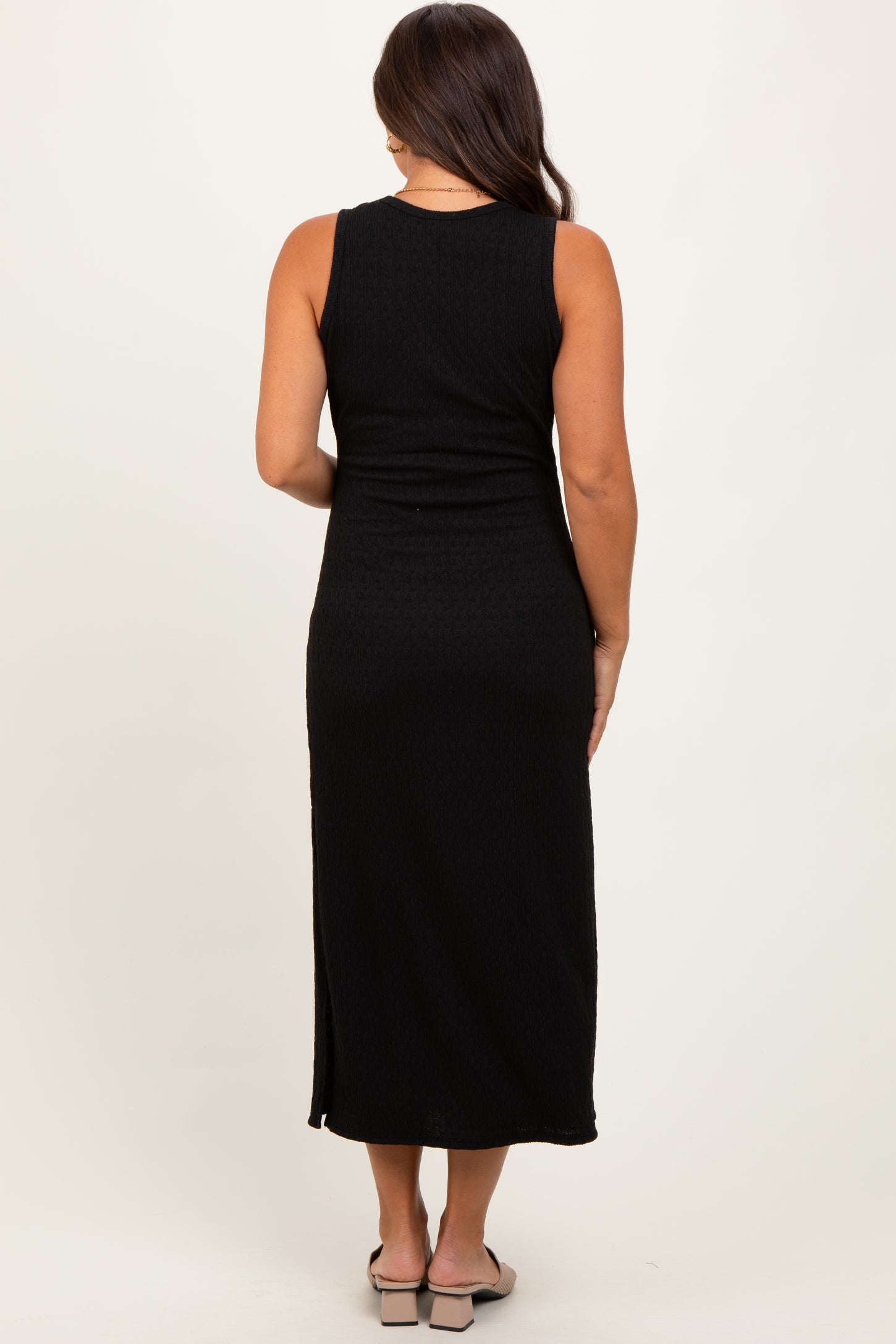 woman wearing a black sleeveless maternity maxi dress, showing a fitted silhouette and long length from the back
