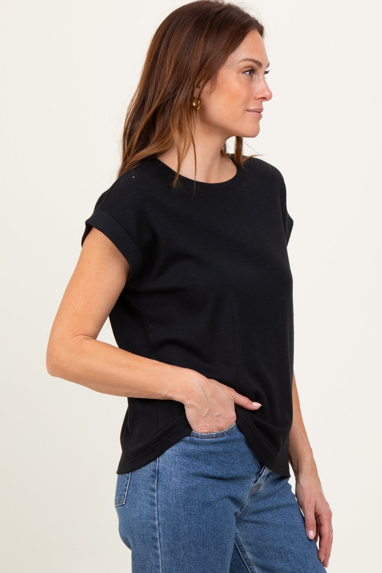 woman wearing a black short sleeve crew neck top with rolled cuffs and side slits, paired with blue jeans