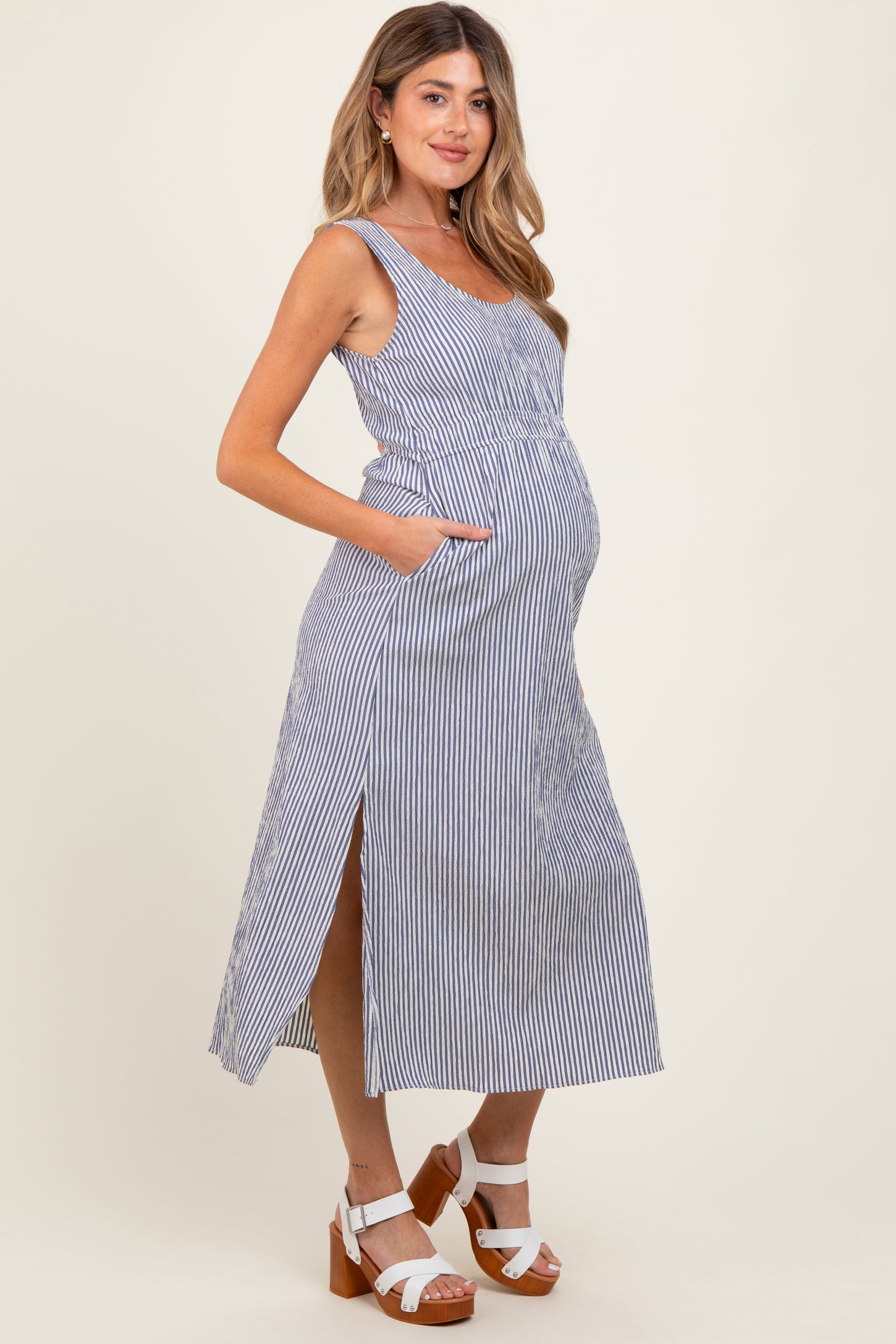 woman wearing a blue and white striped maternity maxi dress with pockets and side slits, showing her baby bump