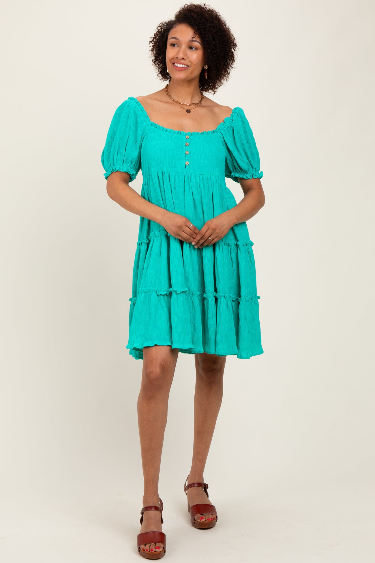 woman wearing a teal short sleeve tiered dress with buttons and puffed sleeves, standing against a neutral background