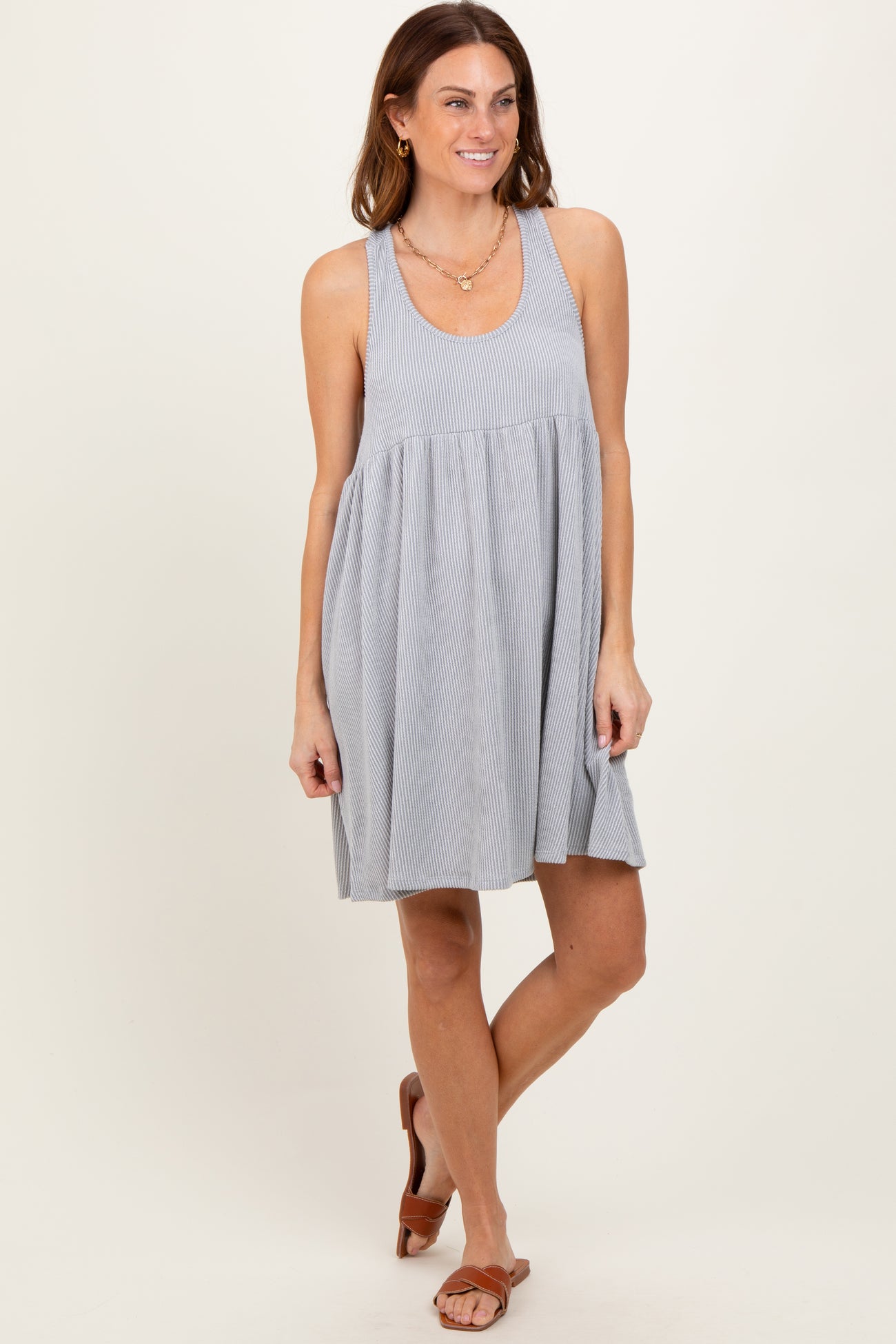 woman wearing a gray striped sleeveless swing dress and brown sandals, standing against a neutral background