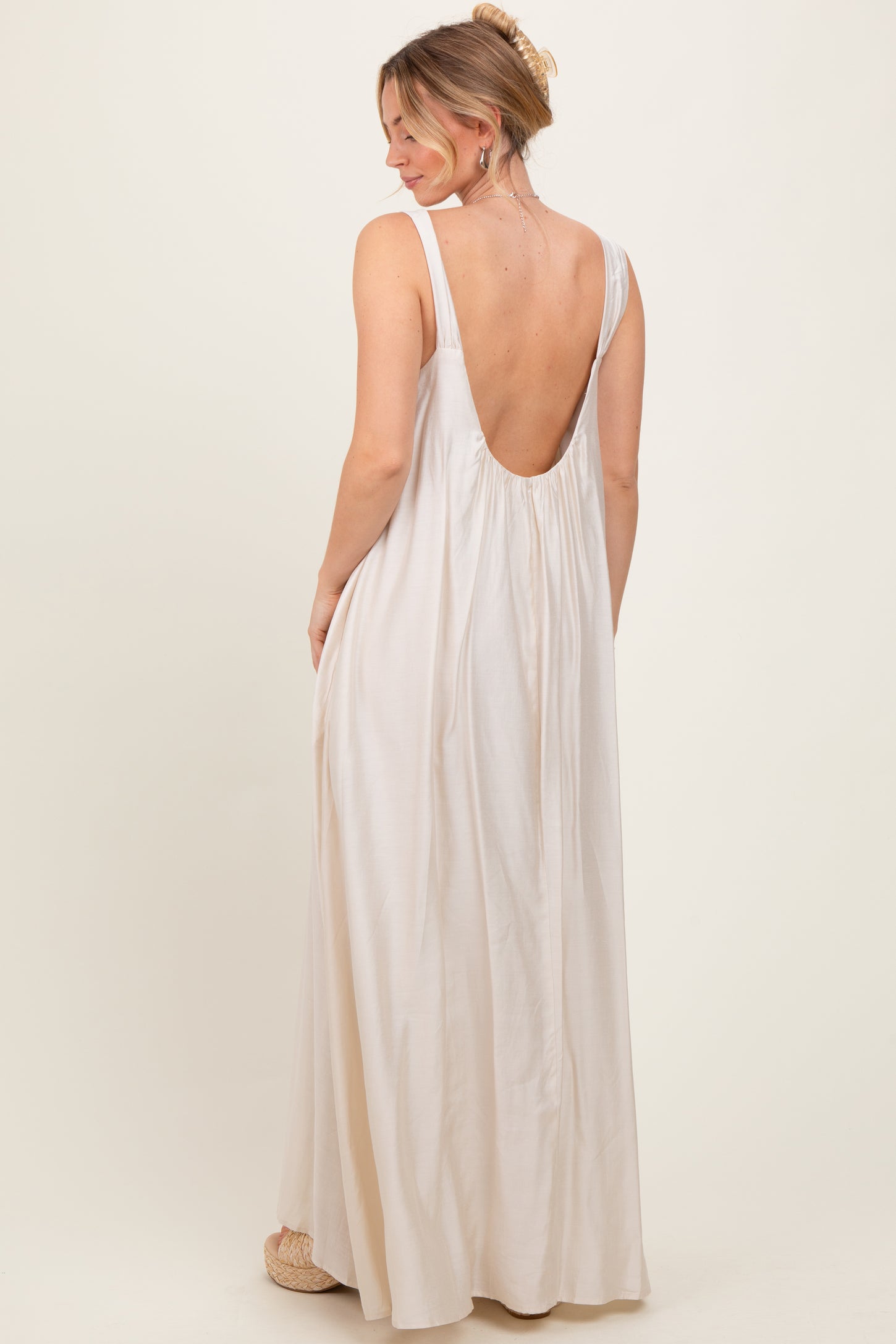 woman wearing a natural-colored backless maxi dress with a flowy silhouette and a relaxed fit