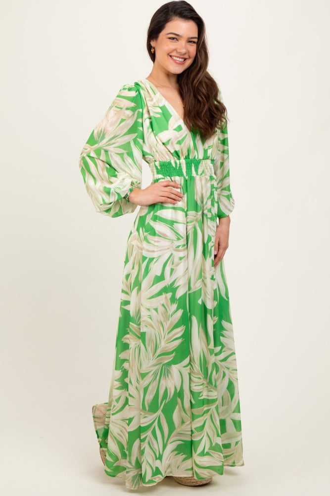 woman wearing a green maxi dress with a tropical leaf print and puff sleeves, styled with a smocked waist