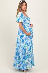 woman wearing a floral maternity maxi dress in blue and white, holding her baby bump