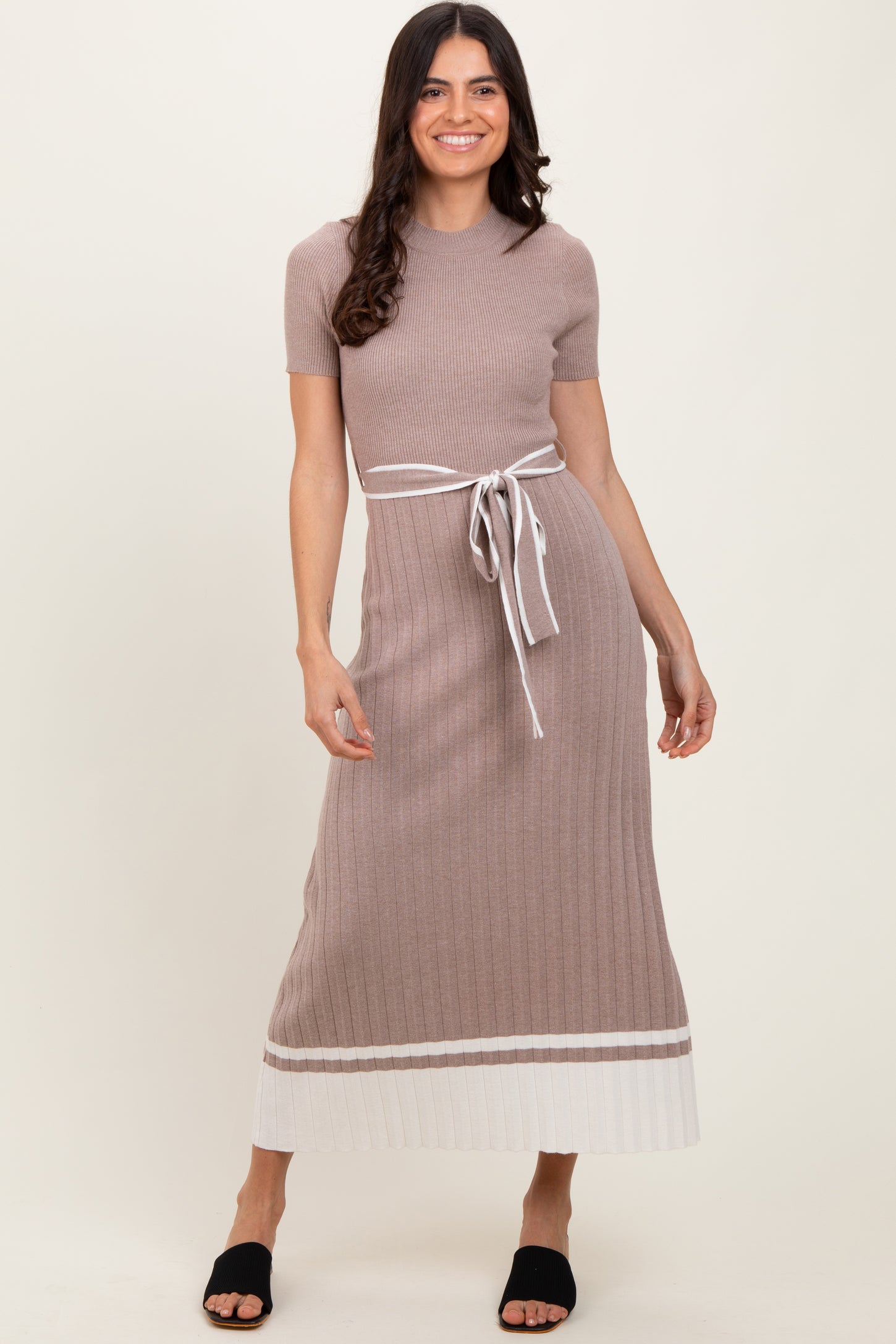 woman wearing a beige ribbed maxi dress with a tie belt and contrasting white hem detail, standing in a relaxed pose