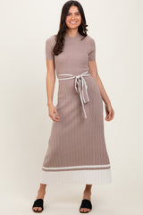 woman wearing a beige ribbed maxi dress with a tie belt and contrasting white hem detail, standing in a relaxed pose