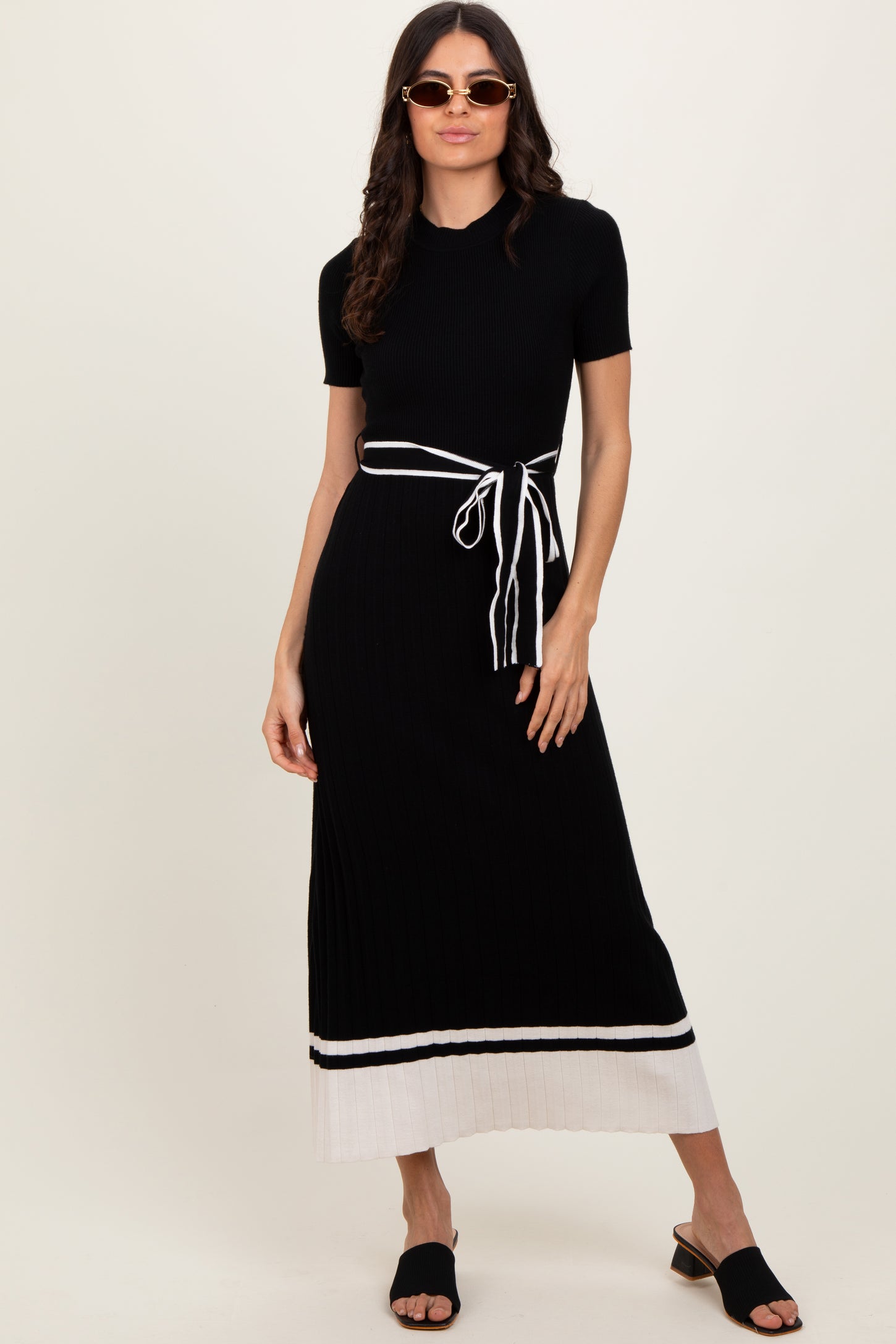 woman wearing a black ribbed knit maxi dress with a white striped hem and a tie waist detail, paired with sunglasses