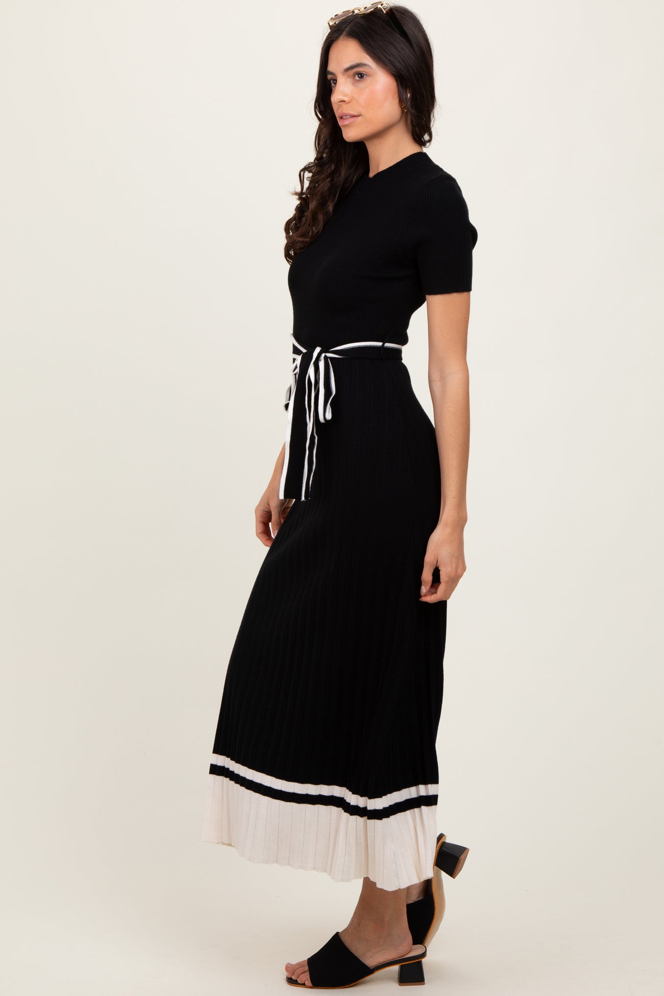 woman wearing a black ribbed maxi dress with a tie waist and white striped hem, styled with heels