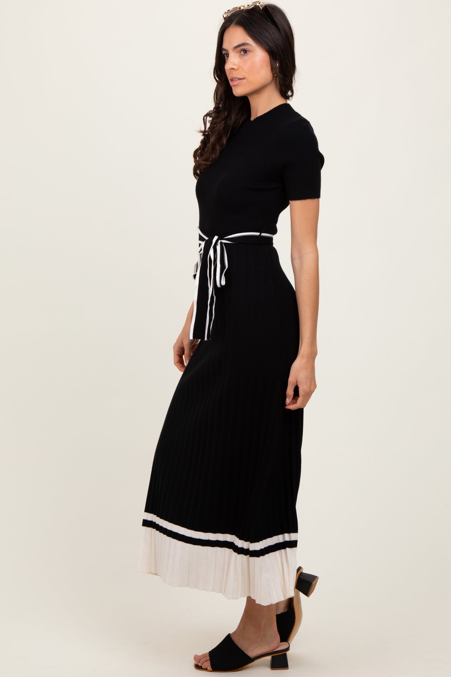 woman wearing a black ribbed maxi dress with a tie waist and white striped hem, styled with heels
