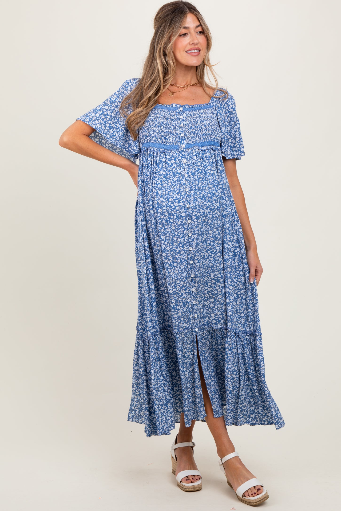 woman wearing a blue floral maternity dress with short sleeves and a button-down detail, featuring a tiered skirt