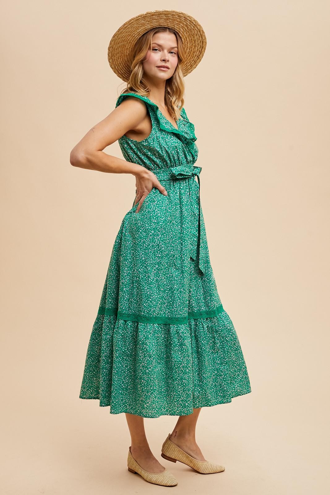 woman wearing a green floral midi dress with ruffled neckline and tie waist, styled with a straw hat and espadrilles