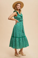 woman wearing a green floral midi dress with ruffled neckline and tie waist, styled with a straw hat and espadrilles