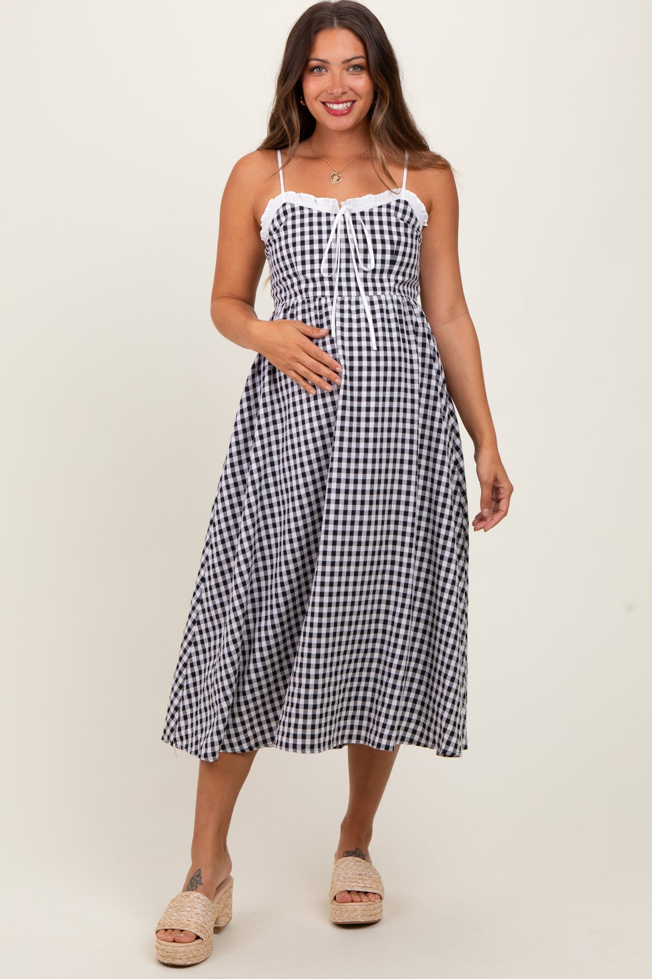 woman wearing a black and white gingham maternity dress with lace trim and holding her baby bump