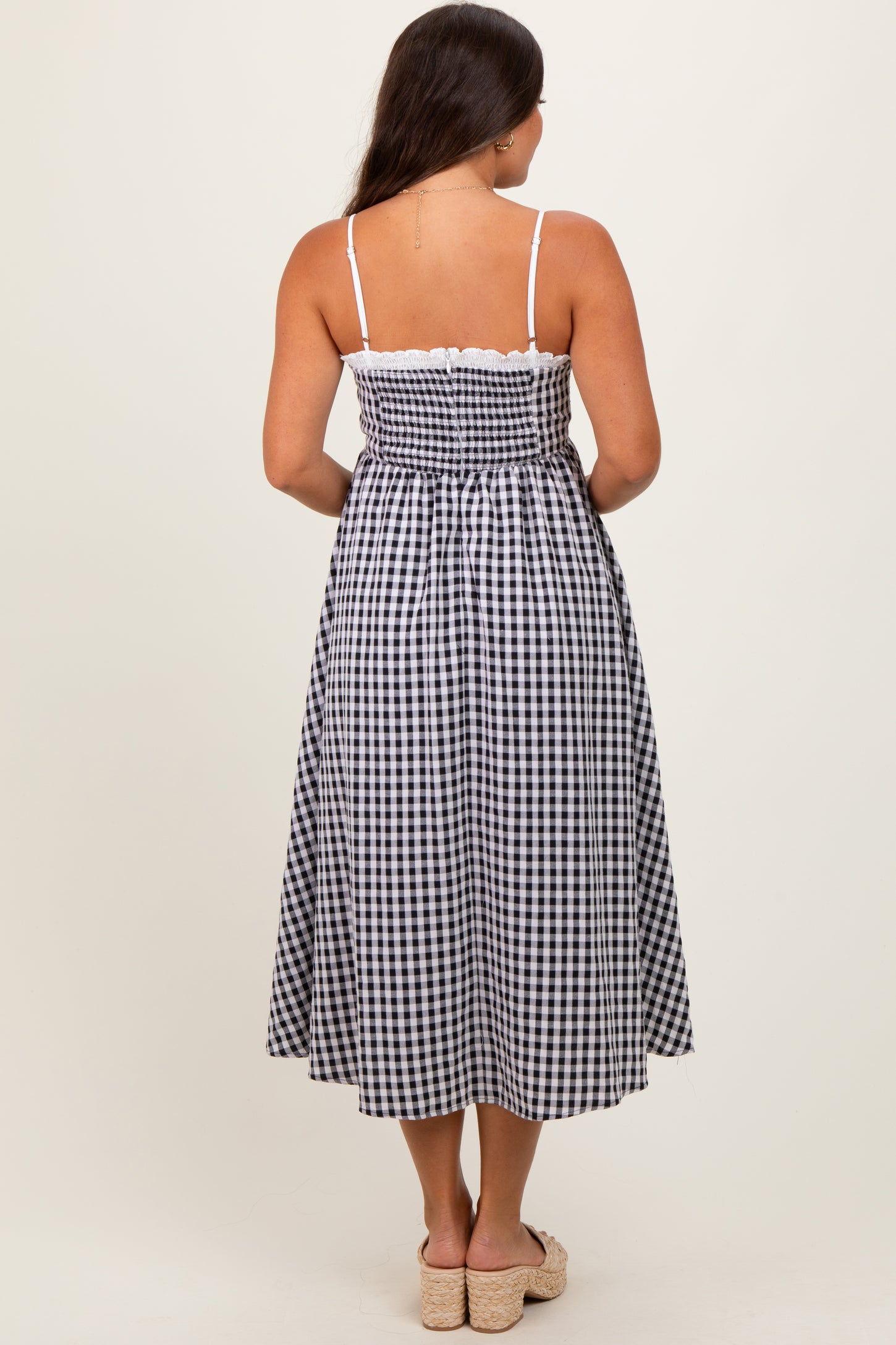 woman wearing a black and white gingham maternity maxi dress with spaghetti straps and a smocked back
