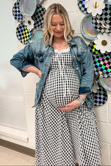 woman wearing a black and white gingham maternity dress with a denim jacket and holding her baby bump