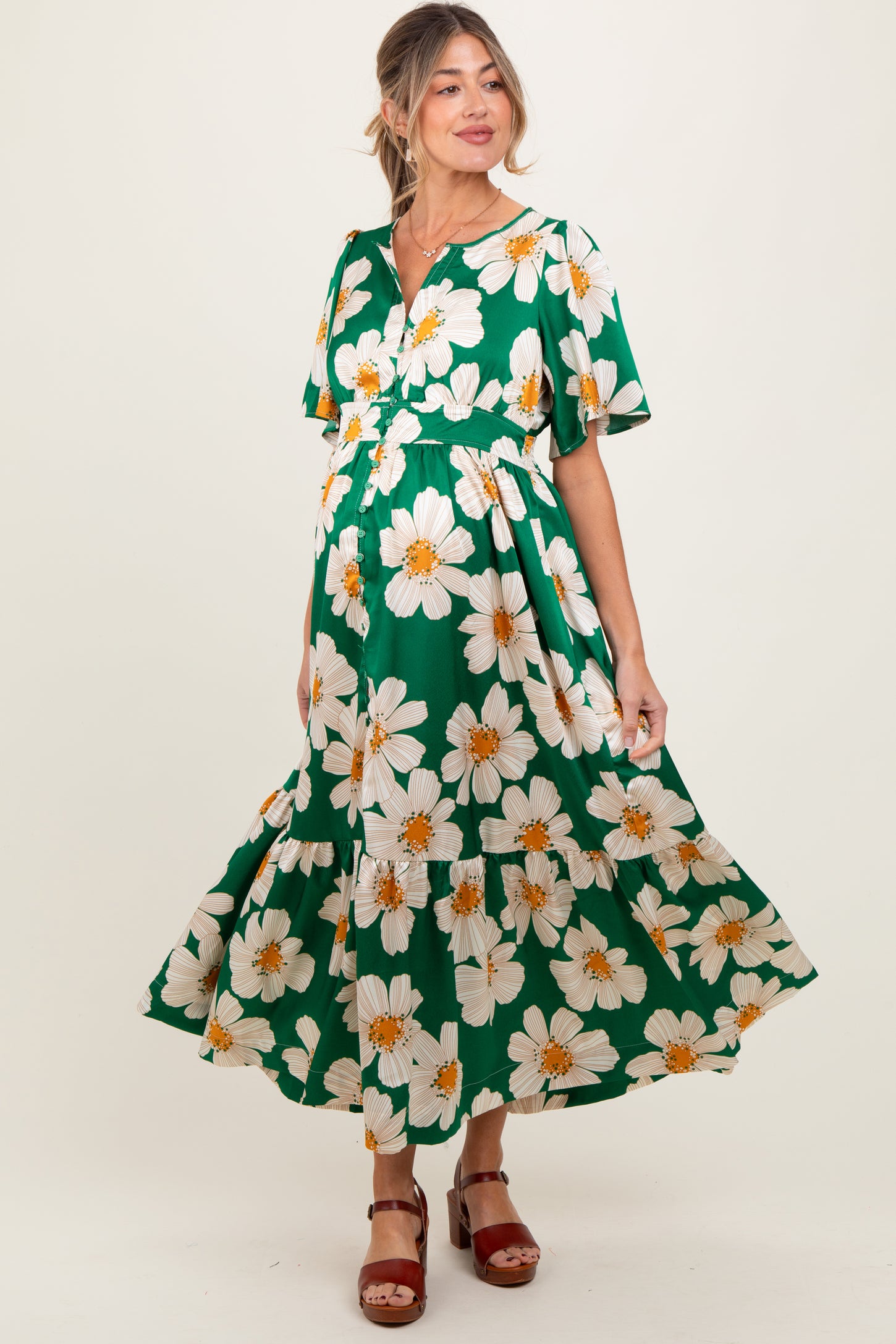 woman wearing a green floral maternity maxi dress with short sleeves and a tiered skirt, showing her baby bump