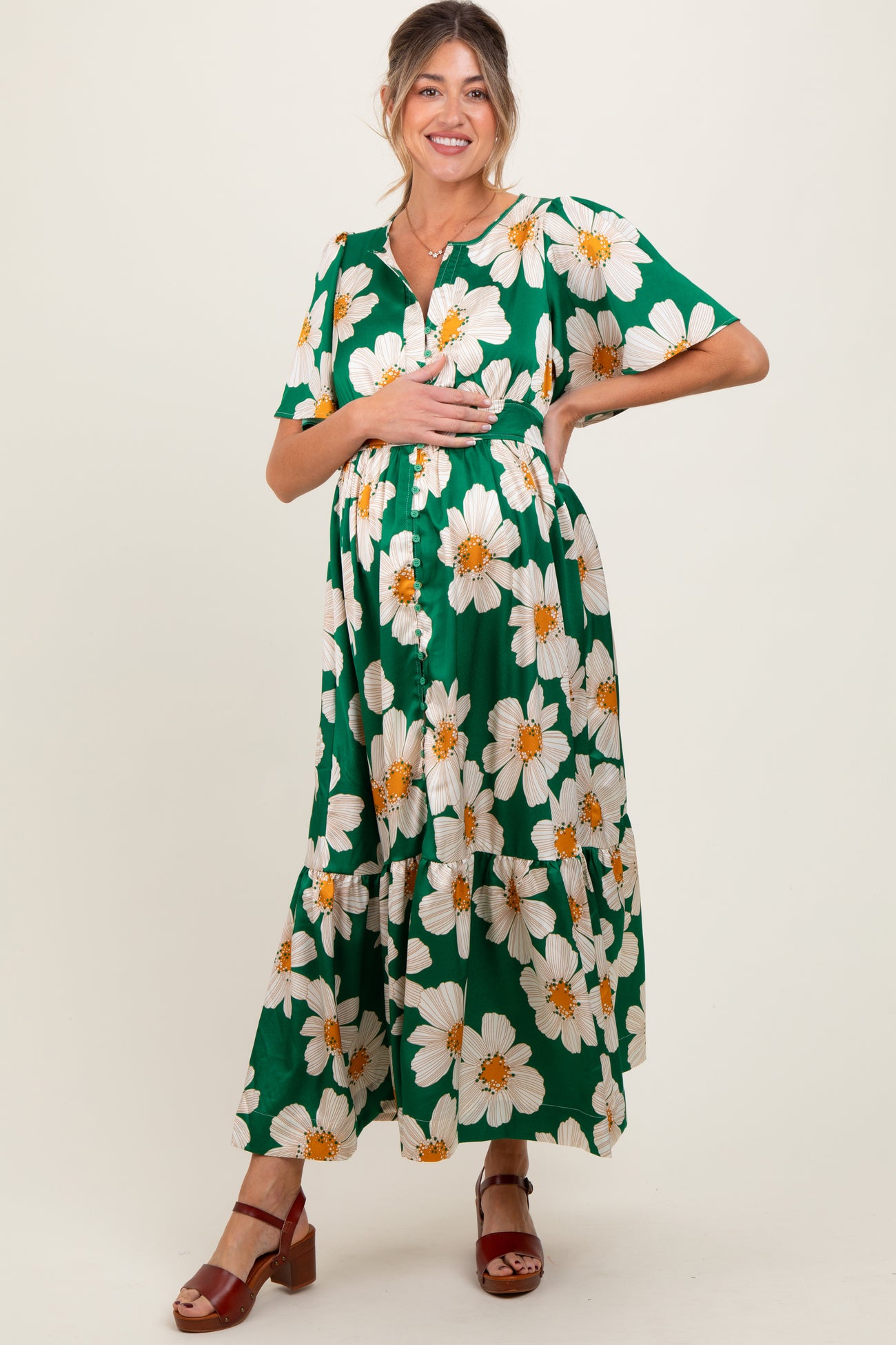 woman wearing a green floral maternity maxi dress and holding her baby bump