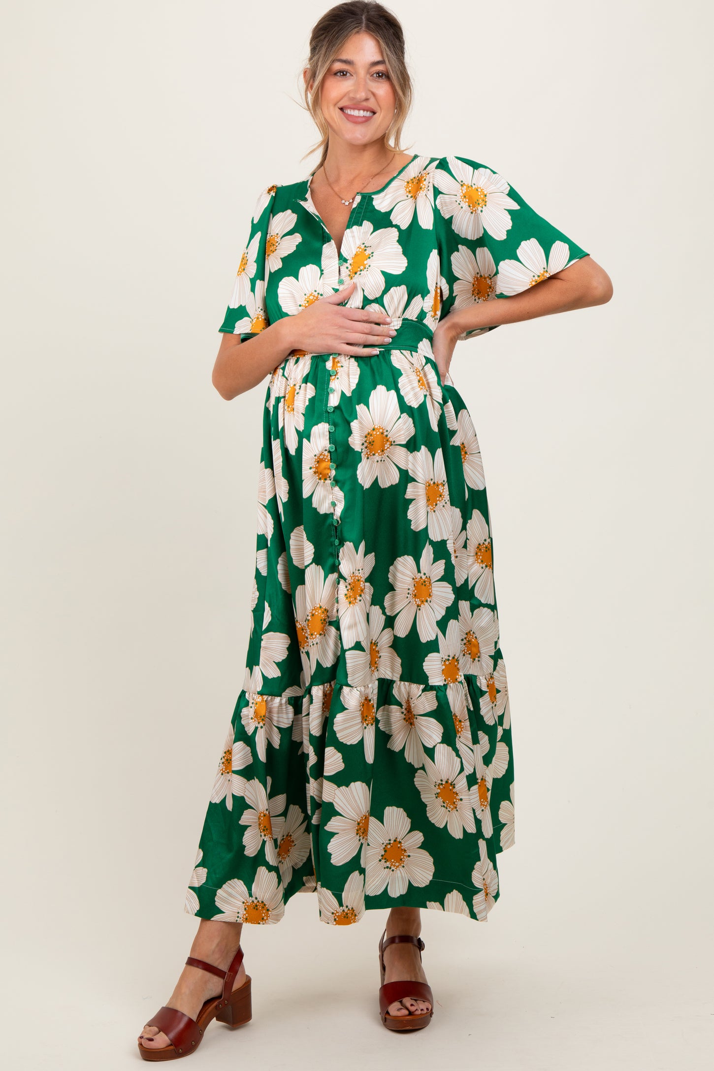 woman wearing a green floral maternity maxi dress and holding her baby bump