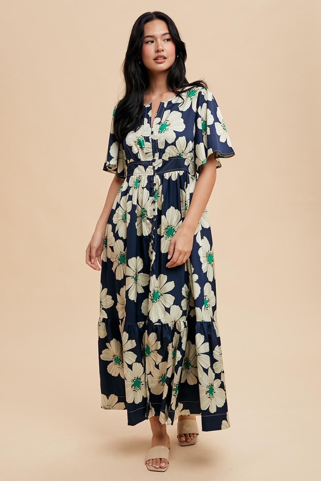 woman wearing a navy floral maxi dress with short sleeves and a cinched waist, standing on a neutral background