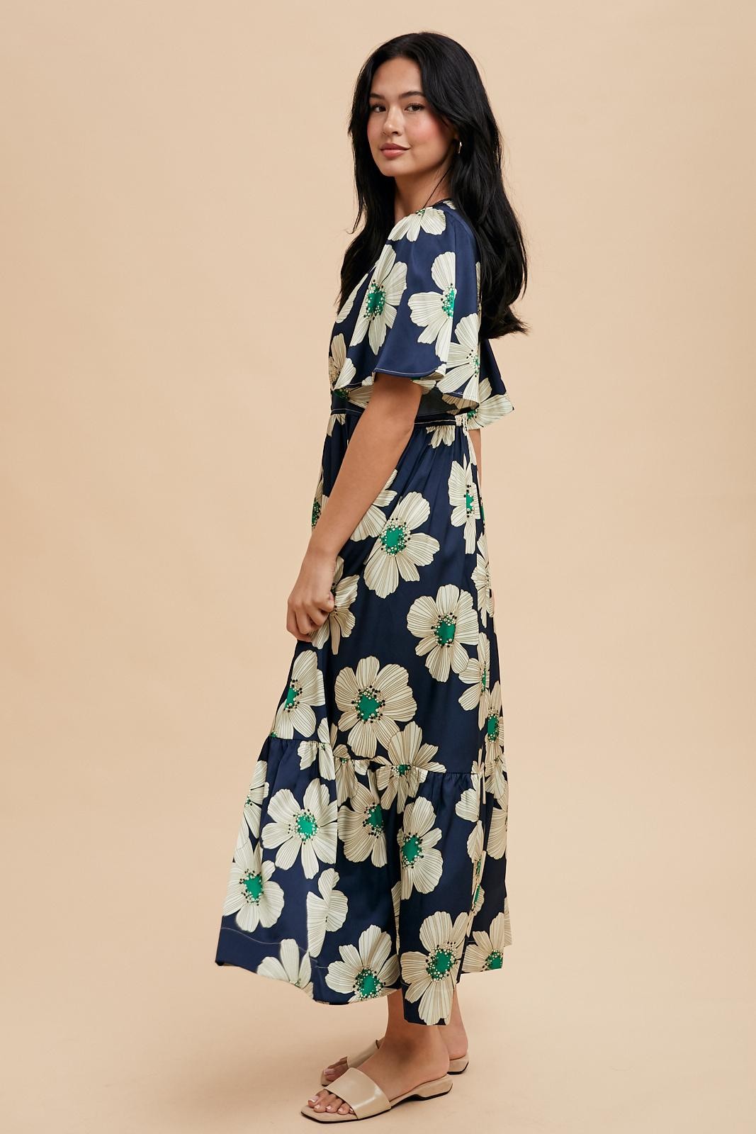 woman wearing a navy floral maxi dress with flutter sleeves and a tie waist, standing against a neutral background